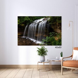 May include: A photograph of a waterfall cascading down a rocky cliff face, surrounded by lush green foliage. The waterfall is in focus, with the surrounding greenery blurred in the background. The image is framed with a white border and the text "40x60" is printed in the bottom right corner.
