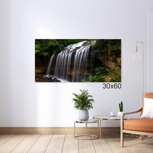 May include: A photograph of a waterfall cascading over a rocky cliff, surrounded by lush green foliage. The waterfall is a beautiful natural feature, with the water flowing over the rocks and creating a misty spray. The image is taken from a low angle, giving the viewer a sense of the height and power of the waterfall.