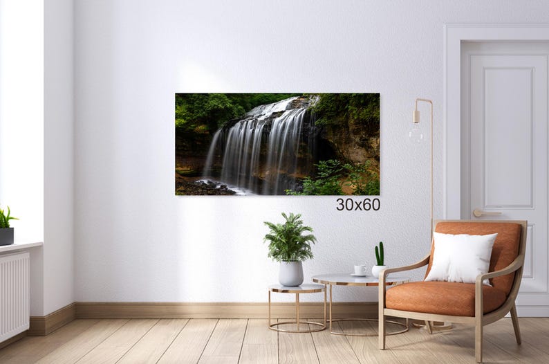 May include: A photograph of a waterfall cascading over a rocky cliff, surrounded by lush green foliage. The waterfall is a beautiful natural feature, with the water flowing over the rocks and creating a misty spray. The image is taken from a low angle, giving the viewer a sense of the height and power of the waterfall.