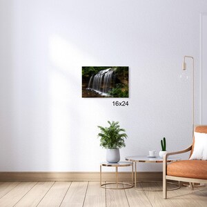 May include: A photograph of a waterfall cascading over rocks in a lush green forest. The water is clear and flowing over the rocks, creating a beautiful natural scene. The image is taken from a low angle, giving the viewer a sense of the height of the waterfall.