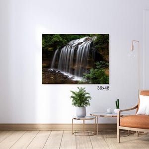 May include: A photograph of a waterfall cascading down a rocky cliff face, surrounded by lush green foliage. The water is white and foamy, and the rocks are brown and gray. The image is taken from a low angle, looking up at the waterfall.