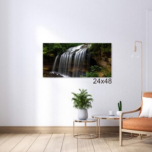 May include: A photograph of a waterfall cascading over rocks and greenery. The waterfall is surrounded by lush foliage and the water is flowing over the rocks in a smooth, continuous stream. The image is taken from a low angle, giving the viewer a sense of the height and power of the waterfall.