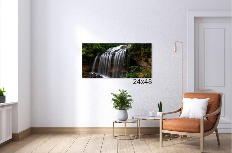 May include: A photograph of a waterfall cascading over rocks and greenery. The waterfall is surrounded by lush foliage and the water is flowing over the rocks in a smooth, continuous stream. The image is taken from a low angle, giving the viewer a sense of the height and power of the waterfall.