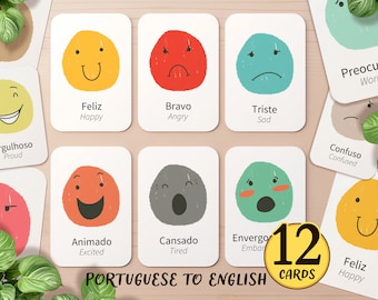 May include: 12 flashcards with colourful illustrations of different emotions. Each card features a Portuguese word and its English translation. The words include: "Feliz", "Bravo", "Triste", "Orgulhoso", "Animado", "Cansado", "Envergonhado", "Preocupado", "Confuso", and more.