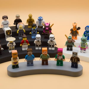May include: A collection of colorful Lego minifigures, including characters from Star Wars, Minecraft, and other themes. The figures are arranged on tiered display stands against a light orange background.
