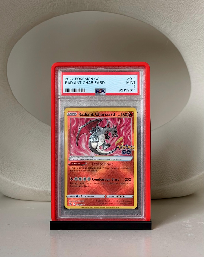 May include: A graded 2022 Pok&eacute;mon GO Radiant Charizard card in a red case. The card features a fiery background and a depiction of Charizard. The card is graded as Mint 9 by PSA, with the number 92192611.