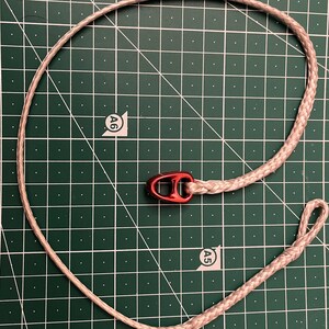Può includere: Una corda bianca con un fermaglio di metallo rosso. La corda è su un tappetino da taglio verde con segni bianchi.