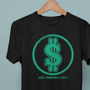 以下が含まれることがあります： 円の中に緑色のドルマークが描かれた黒いTシャツで、その下に「PAY YOURSELF FIRST」という文字が書かれています。