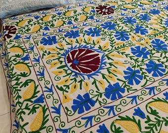 Cubrecama tradicional de algodón bordado a mano con llamativos motivos florales y de hojas en tonos azul, amarillo y granate.