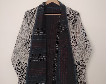 Könnte beinhalten: Wende-Kimono-Jacke mit einem schwarz-weißen Paisley-Muster auf der Außenseite. Die Innenseite ist schwarz mit vertikalen Nähten in Weiß, Rot und Blau. Die Jacke hängt an einem Holzbügel.