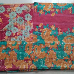 May include: A kantha quilt with a floral pattern in shades of red, orange, green, and white. The quilt is made of recycled saris and is hand-stitched.