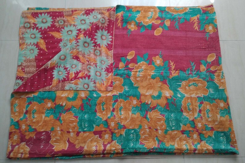 May include: A kantha quilt with a floral pattern in shades of red, orange, green, and white. The quilt is made of recycled saris and is hand-stitched.