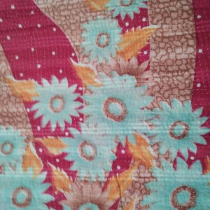 May include: A close-up of a fabric with a floral pattern. The fabric is red with white dots and features a repeating pattern of blue and yellow flowers.