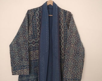 Könnte beinhalten: Eine blaue gesteppte Jacke mit geometrischem Muster. Die Jacke hat einen Schalkragen und ein langes, fließendes Design.