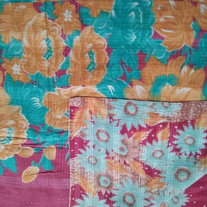 May include: A kantha quilt with a floral pattern in shades of orange, teal, and pink. The quilt is made of recycled saris and is hand-stitched.
