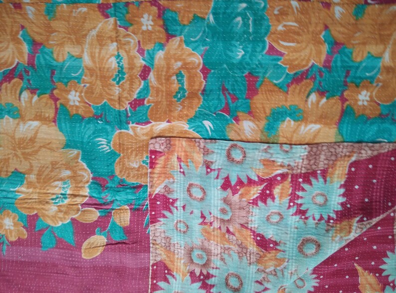 May include: A kantha quilt with a floral pattern in shades of orange, teal, and pink. The quilt is made of recycled saris and is hand-stitched.