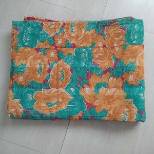 May include: A folded floral patterned blanket in shades of green, orange, and red.