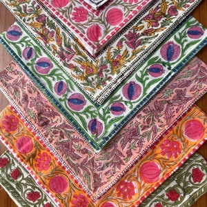 Puede incluir: Una pila de seis servilletas de tela coloridas con patrones florales y un borde de color rosa, naranja y verde. Las servilletas están dobladas en forma triangular y dispuestas en forma de pirámide.