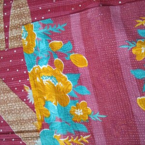 May include: A pink kantha quilt with a floral pattern in shades of yellow, turquoise, and white. The quilt has a white polka dot pattern on the pink background.