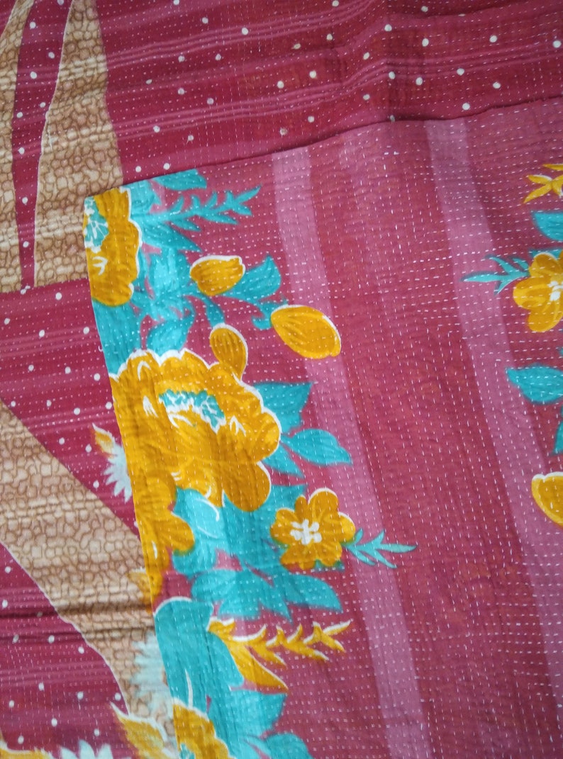 May include: A pink kantha quilt with a floral pattern in shades of yellow, turquoise, and white. The quilt has a white polka dot pattern on the pink background.