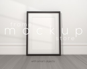 May include: A black picture frame mockup with a white mat and a white background. The frame is sitting on a gray wood floor.