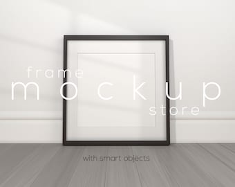 May include: A black picture frame with a white mat and a white background. The frame is sitting on a gray wood floor. The text "frame mockup store" is written in white on the wall behind the frame. The text "with smart objects" is written in white below the frame.
