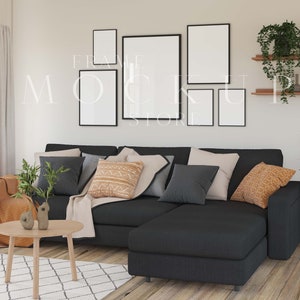 May include: A black sectional sofa with a variety of throw pillows in a living room setting. The sofa is positioned in front of a wall with four black framed pictures. The pictures are arranged in a grid pattern. There is a wooden shelf with plants on the wall to the right of the sofa.