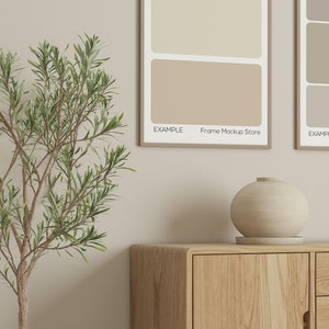 May include: A wooden cabinet with a rounded edge and a light-colored, spherical vase on top. Two framed art prints with neutral color swatches hang on the wall. The text "EXAMPLE Frame Mockup Store" is visible on the prints.