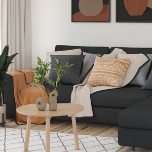 May include: A black sectional sofa with a beige throw blanket and a patterned cushion. Two small ceramic vases with green plants are on a round wooden coffee table in front of the sofa.