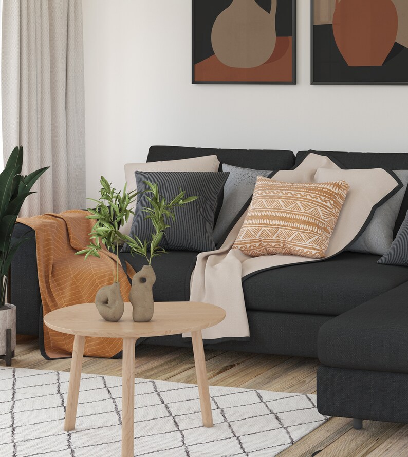 May include: A black sectional sofa with a beige throw blanket and a patterned cushion. Two small ceramic vases with green plants are on a round wooden coffee table in front of the sofa.