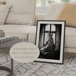 May include: A black and white photograph of a sculpture of two figures embracing, framed in a black frame. The sculpture is set against a window with a view of a building.
