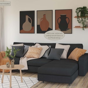May include: A sectional sofa with a chaise lounge in a dark grey fabric. The sofa is decorated with throw pillows in various colours and patterns, including a brown and white patterned pillow, a grey pillow, and a beige pillow. There are two small decorative objects on a wooden coffee table in front of the sofa. The wall behind the sofa is decorated with three framed abstract art prints featuring vases in shades of brown, beige, and black. The text "Add your artwork using smart layers in Photoshop" is visible in the image.