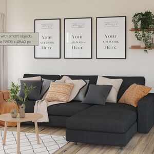 May include: A black sectional sofa with a chaise lounge, featuring a variety of throw pillows in shades of grey, beige, and orange. The sofa is positioned in front of a white wall with three black framed posters that say "Your Artwork Here".
