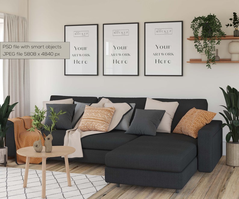 May include: A black sectional sofa with a chaise lounge, featuring a variety of throw pillows in shades of grey, beige, and orange. The sofa is positioned in front of a white wall with three black framed posters that say "Your Artwork Here".