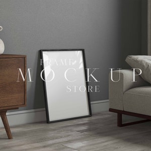 May include: A black picture frame mockup on a wooden table in a living room setting. The frame is empty and ready for your design.  FRAME MOCKUP STORE