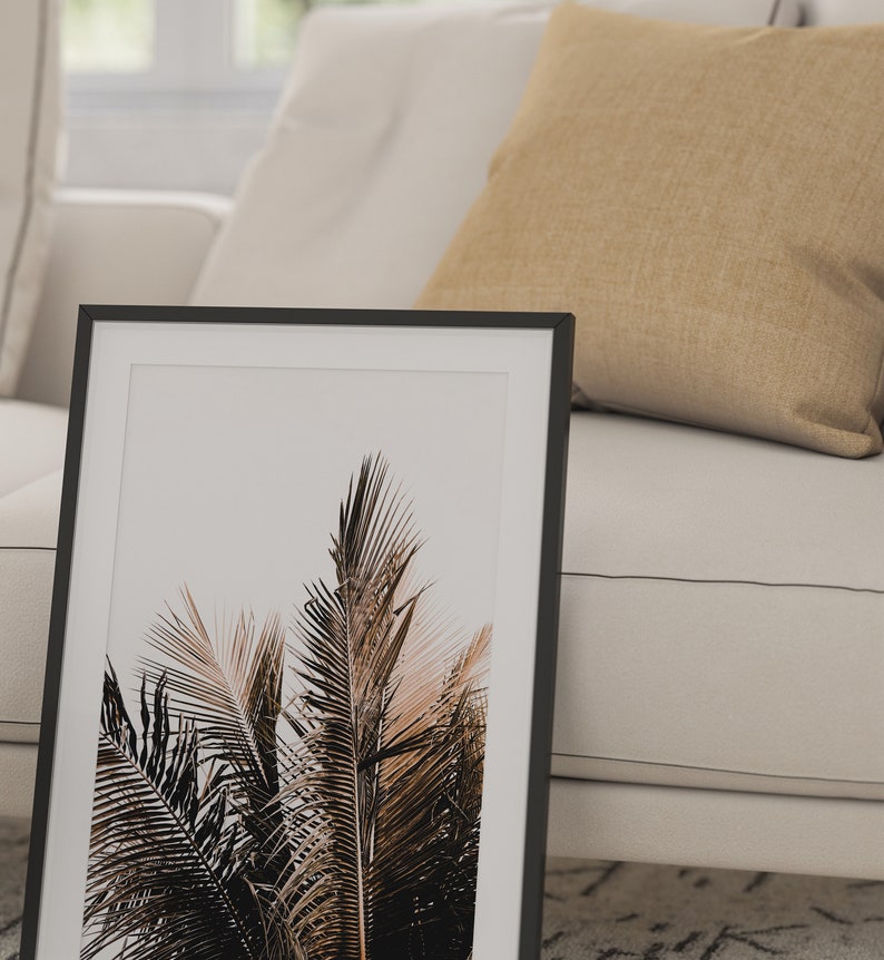 May include: A black framed print of a close-up of palm tree leaves against a white background.