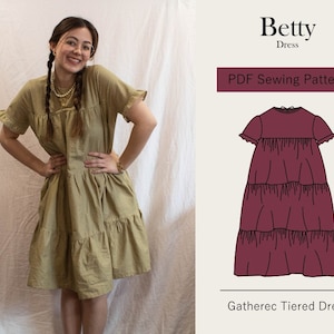 May include: A PDF sewing pattern for a gathered tiered dress called "Betty Dress". The pattern shows a burgundy dress with a round neckline and short sleeves. The dress has three tiers of fabric.