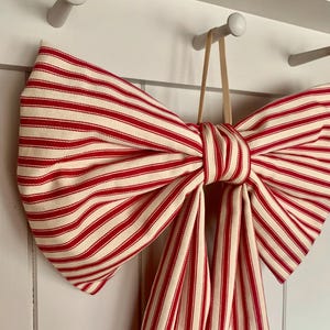 May include: A large red and white striped fabric bow tied with a tan ribbon, hanging from a white hook.
