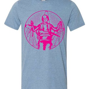 May include: A light blue t-shirt featuring a pink graphic of a person flying a paramotor. The graphic is within a circle with a grid pattern.