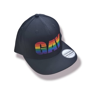 Könnte beinhalten: Schwarze Baseballkappe mit einem regenbogenfarbenen "GAY" Stickerei auf der Vorderseite. Die Kappe hat einen schwarzen verstellbaren Riemen mit einem weißen "Snapback" Etikett.
