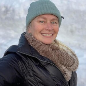 May include: A woman wearing a black puffer jacket with a brown and white knit scarf and a light blue beanie.