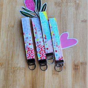 May include: Four colourful keychains with different floral patterns and silver key rings. The keychains are on a wooden surface.