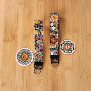May include: Two keychains and two stickers with colorful dot art designs. The keychains have black hardware and a wrist strap. The stickers are round with intricate patterns in shades of red, orange, green, and blue.
