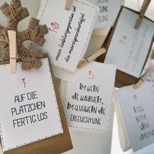 K&ouml;nnte beinhalten: Ein Satz brauner Papiert&uuml;ten mit wei&szlig;en Papierkarten, die daran befestigt sind. Die Karten haben Nummern und Text in deutscher Sprache. Der Text auf den Karten lautet: "Kling Glockchen", "Auf die Pl&auml;tzchen Fertig Los", "Im Wein die Wahrheit, Im Gl&uuml;hwein die Erleuchtung" und "Mein Lieblingsgem&uuml;se ist die Marzipankartoffel".