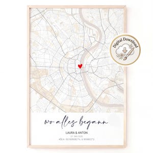 May include: A framed map print featuring a light beige and white street grid with a red heart icon marking a specific location. Below the map, the text reads "wo alles begann", "LAURA & ANTON", "07. MAI 2028", and "KÖLN - 50.939082°N, 6.959802°O".