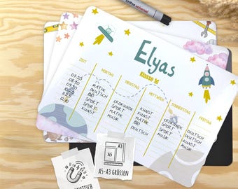 Può includere: Un set di lavagne magnetiche per orari scolastici con il nome "Elyas" e "Klasse 1d" stampati. Le lavagne presentano un layout settimanale con illustrazioni di un razzo, un'astronave e stelle. Una penna nera è appoggiata sopra.
