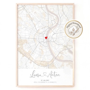 May include: A framed map print of Cologne, Germany, featuring a red heart icon marking a specific location. Below the map, the names Laura and Anton are printed in script, followed by the date 07. JULI 2027 and coordinates 50.939082°N, 6.959802°O.