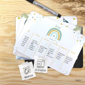 Könnte beinhalten: Ein Stapel weißer, magnetischer Stundenpläne mit Regenbogen-Design, Sternen und dem Namen "Karl". Ein schwarzer Stift liegt obenauf. Die Tafeln zeigen einen Wochenplan mit Fächern wie Mathe und Kunst. In den Größen A5-A3.