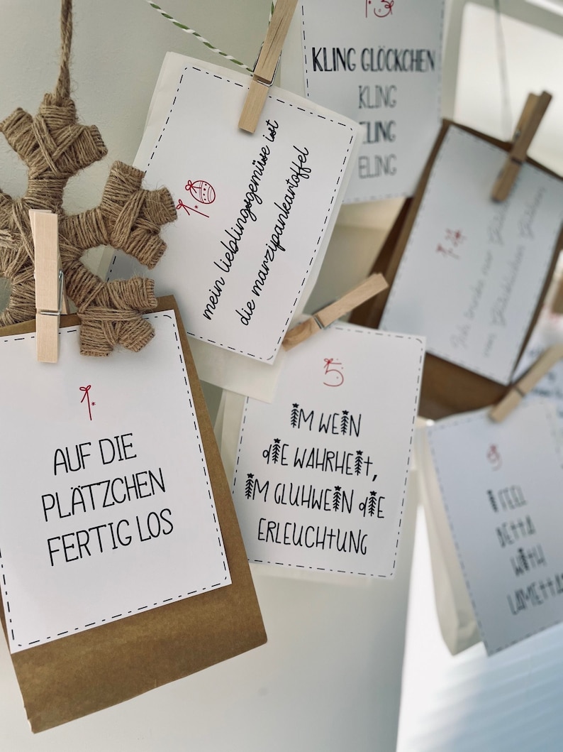 K&ouml;nnte beinhalten: Ein Satz brauner Papiert&uuml;ten mit wei&szlig;en Papierkarten, die daran befestigt sind. Die Karten haben Nummern und Text in deutscher Sprache. Der Text auf den Karten lautet: "Kling Glockchen", "Auf die Pl&auml;tzchen Fertig Los", "Im Wein die Wahrheit, Im Gl&uuml;hwein die Erleuchtung" und "Mein Lieblingsgem&uuml;se ist die Marzipankartoffel".