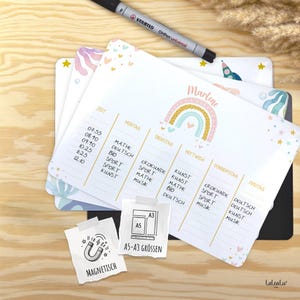 Könnte beinhalten: Weißer magnetischer Stundenplan mit Regenbogen-Design und dem Namen "Marlene". Der Wochenplan enthält Fächer wie Mathe, Kunst und Sport. Ein schwarzer Stift und eine Größenangabe sind ebenfalls zu sehen.